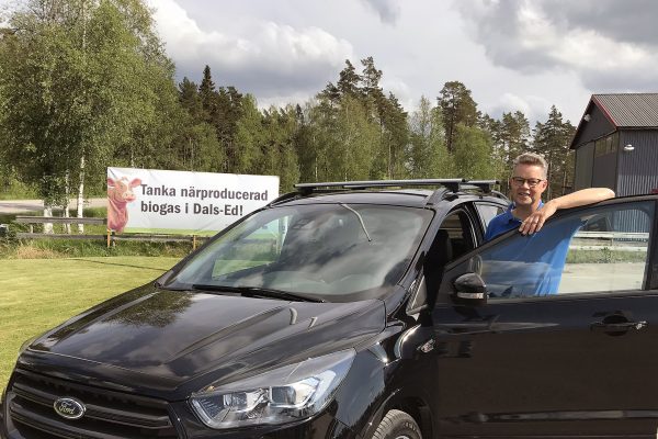 Martin Carling vid en biogasbil framför en skylt med texten "Tanka närproducerad biogas i Dals-Ed".
