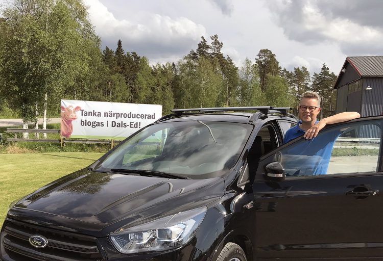 Martin Carling vid en biogasbil framför en skylt med texten "Tanka närproducerad biogas i Dals-Ed".