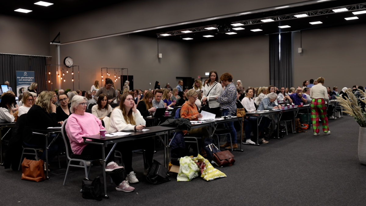 Stor konferenslokal med rader av sittande åhörare.