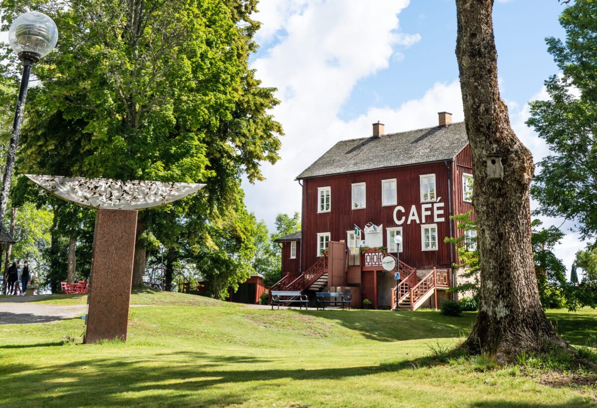 Ett äldre trähus i Dalsland med stor vit skylt som säger "Café". Huset är beläget i en grönskande park.