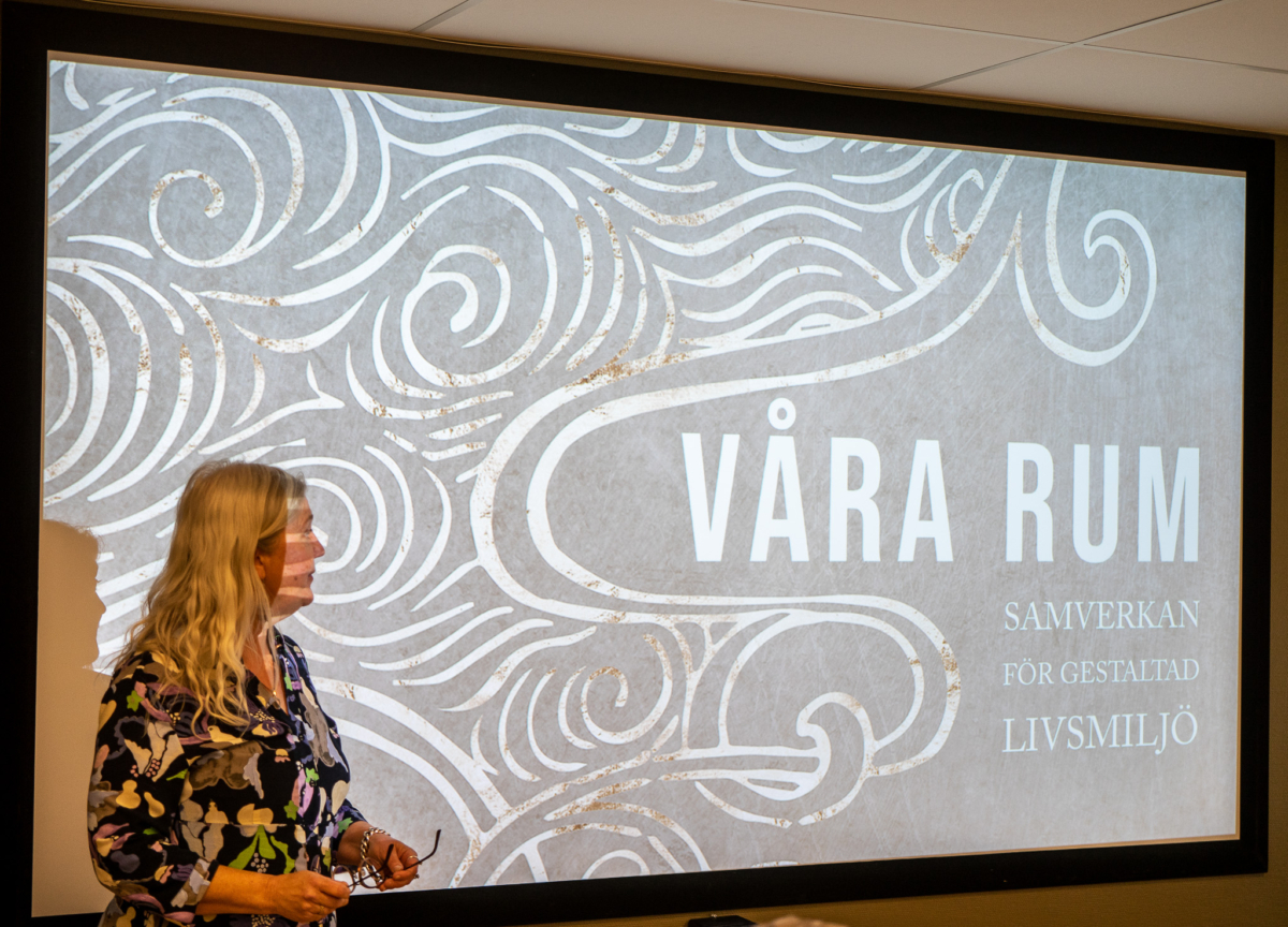 En kvinna står framför en skärm som visar en grafik med texten "Våra rum - samverkan för gestaltad livsmiljö".