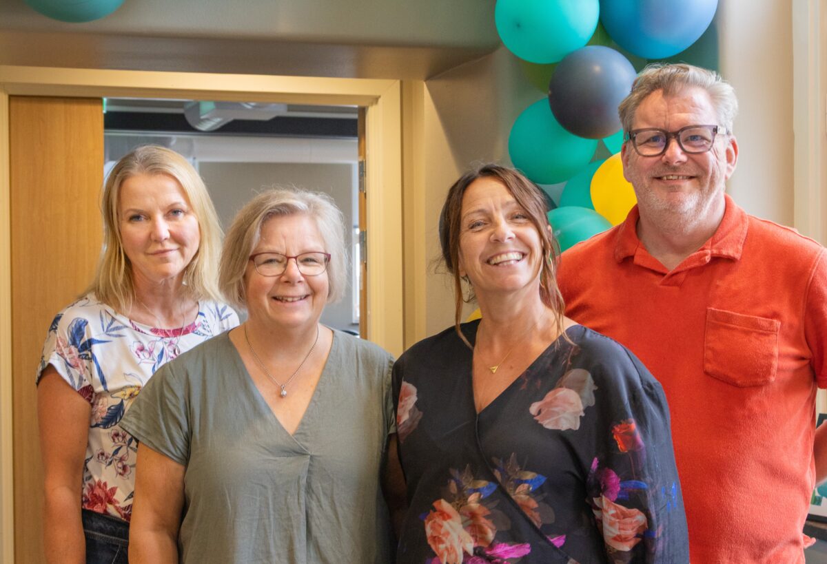 Gruppbild på fyra leende personer med ballonger i bakgrunden.