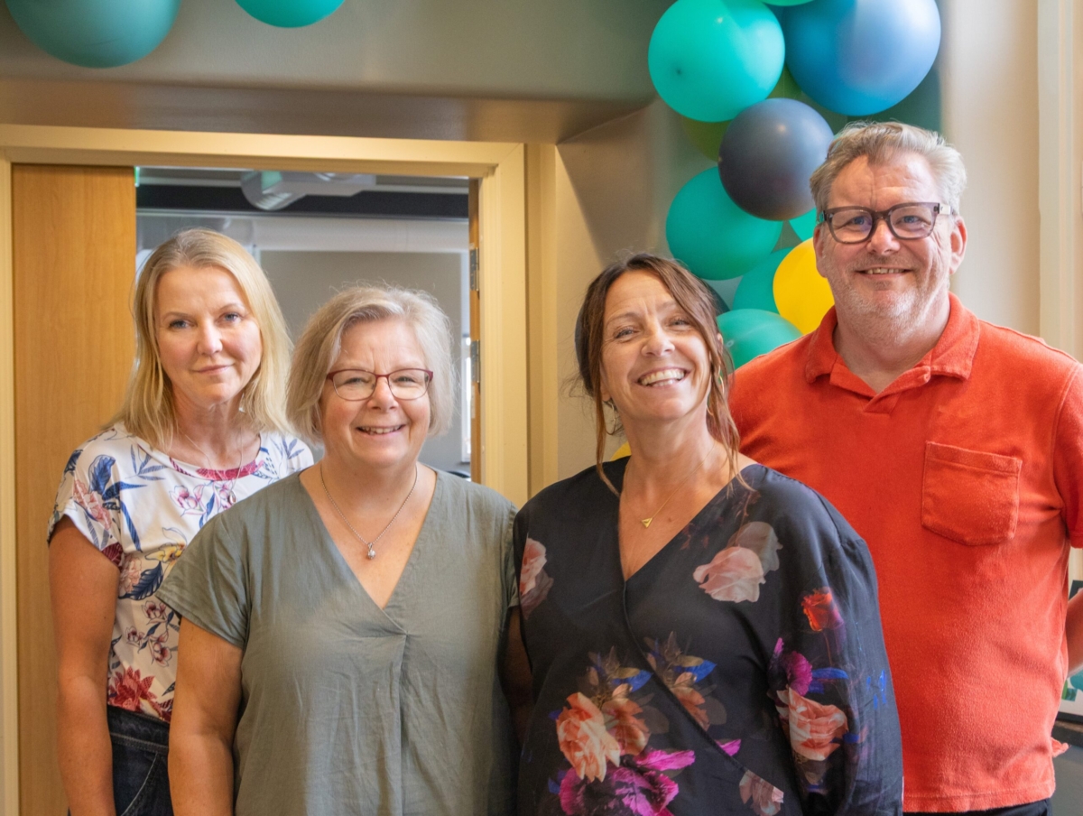 Gruppbild på fyra leende personer med ballonger i bakgrunden.