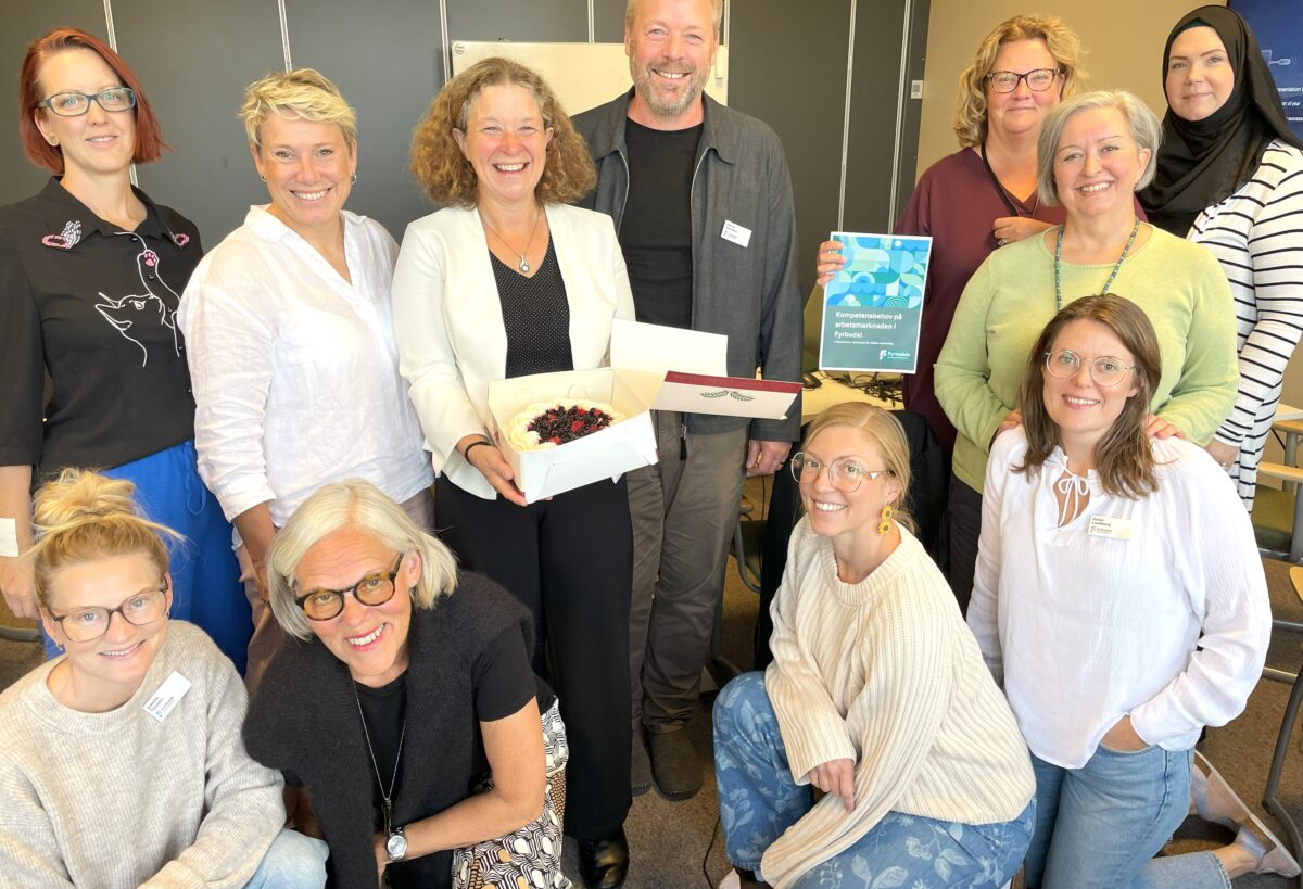 Gruppbild på elva medarbetare från kommunalförbundet. Kvinnan i mitten håller leende i en tårtakartong med tårta. En annan kvinna håller upp en rapport.