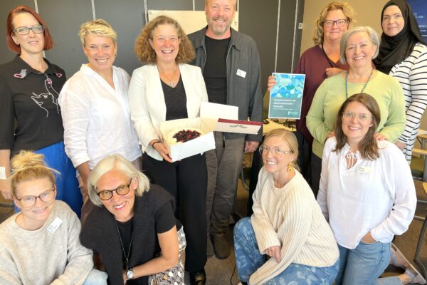 Gruppbild på elva medarbetare från kommunalförbundet. Kvinnan i mitten håller leende i en tårtakartong med tårta. En annan kvinna håller upp en rapport.