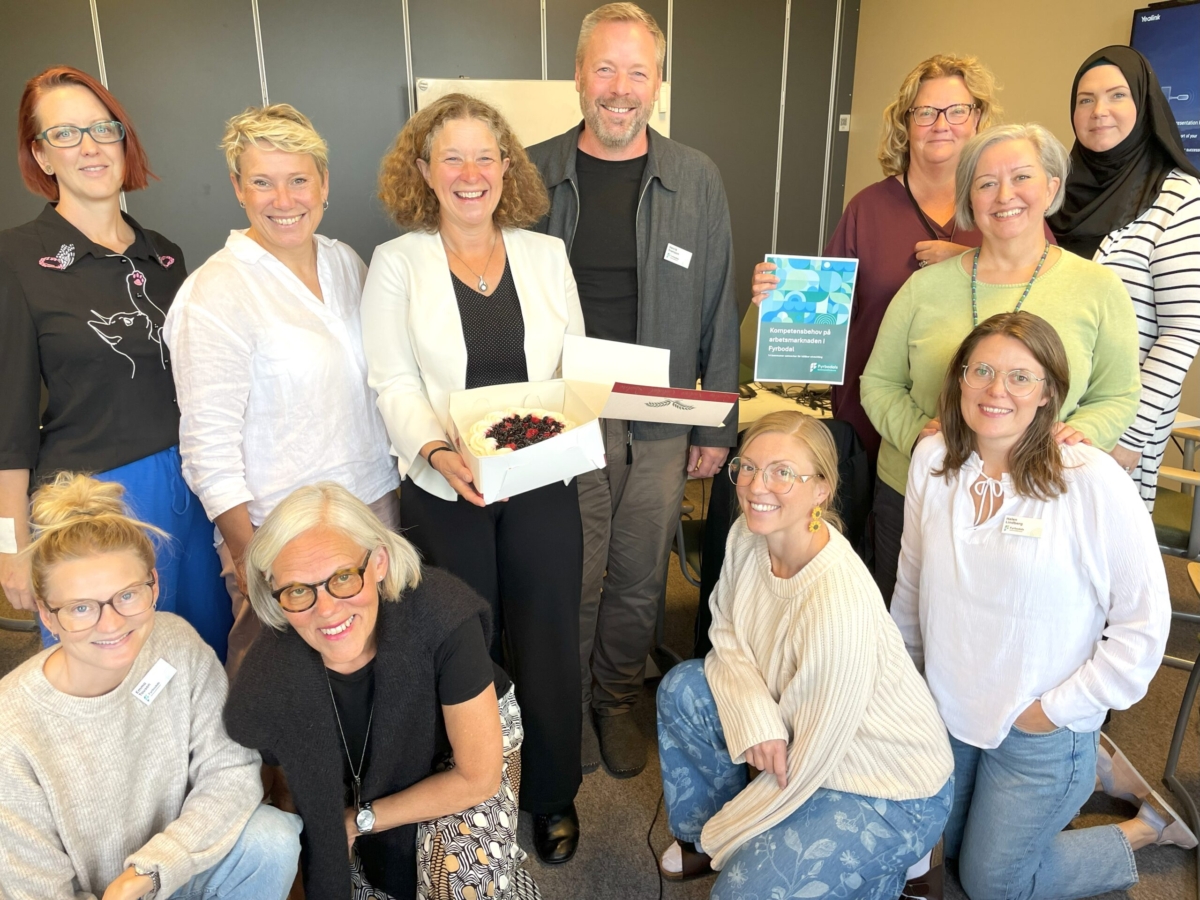 Gruppbild på elva medarbetare från kommunalförbundet. Kvinnan i mitten håller leende i en tårtakartong med tårta. En annan kvinna håller upp en rapport.