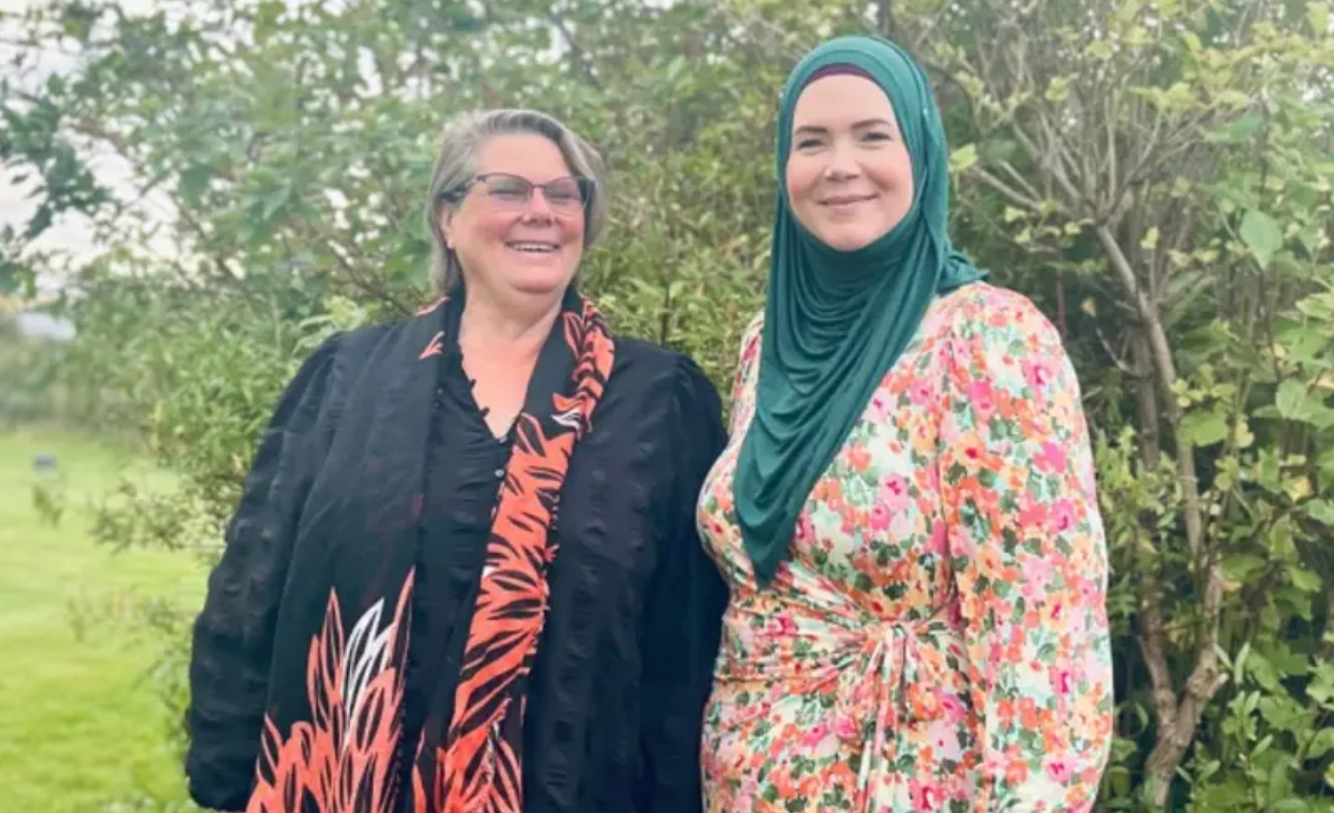 Två leende kvinnor ler in i kameran. I bakgrunden grönska.