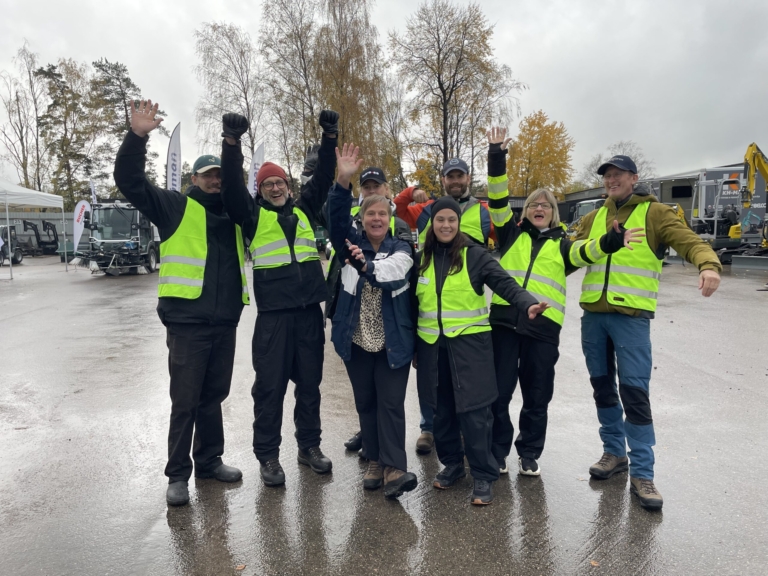 En grupp människor med signaljackor gör segergester och skrattar. I Bakgrunden flera arbetsmaskiner.