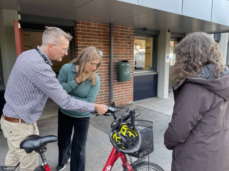 En man och en kvinna undersöker en elcykel medan en annan kvinna tittar på.