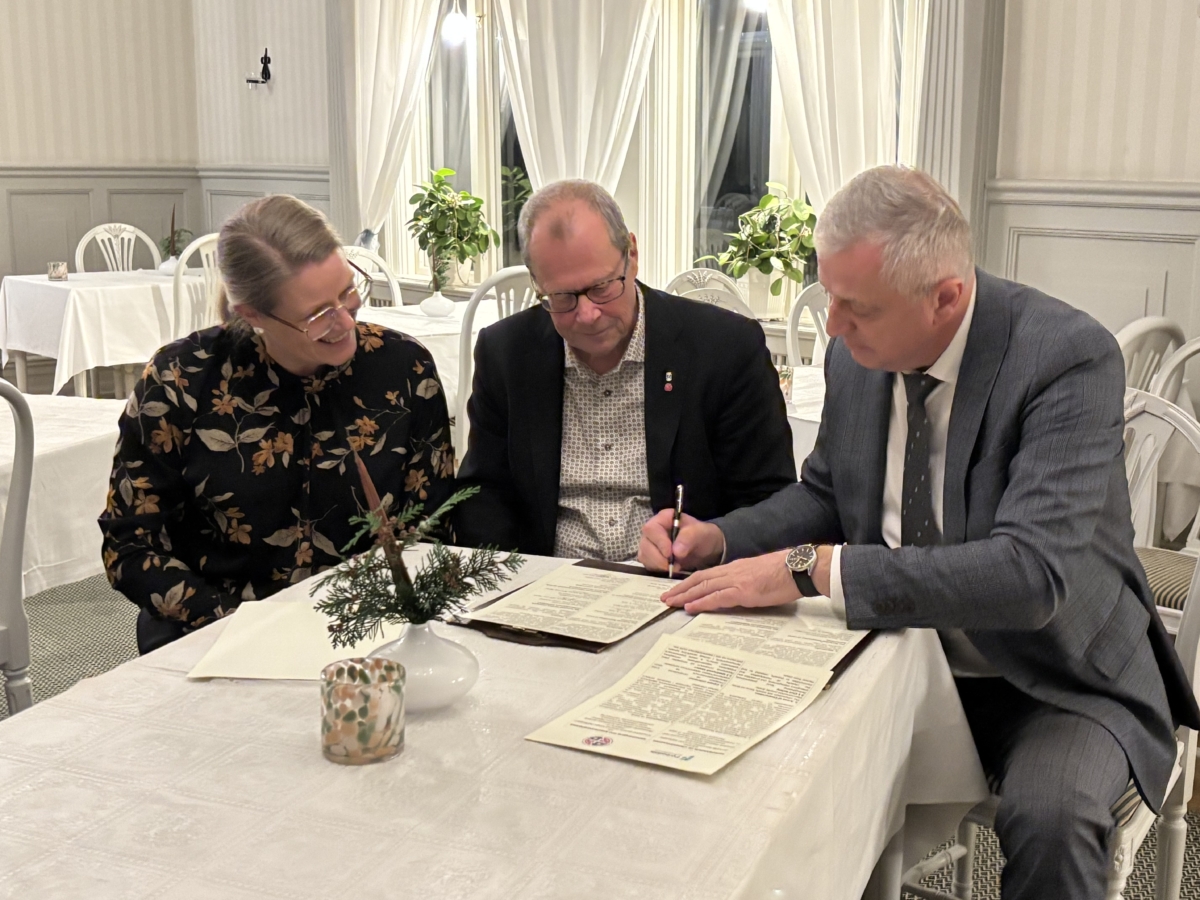 Tre personer sitter vid ett bord och signerar ett dokument.